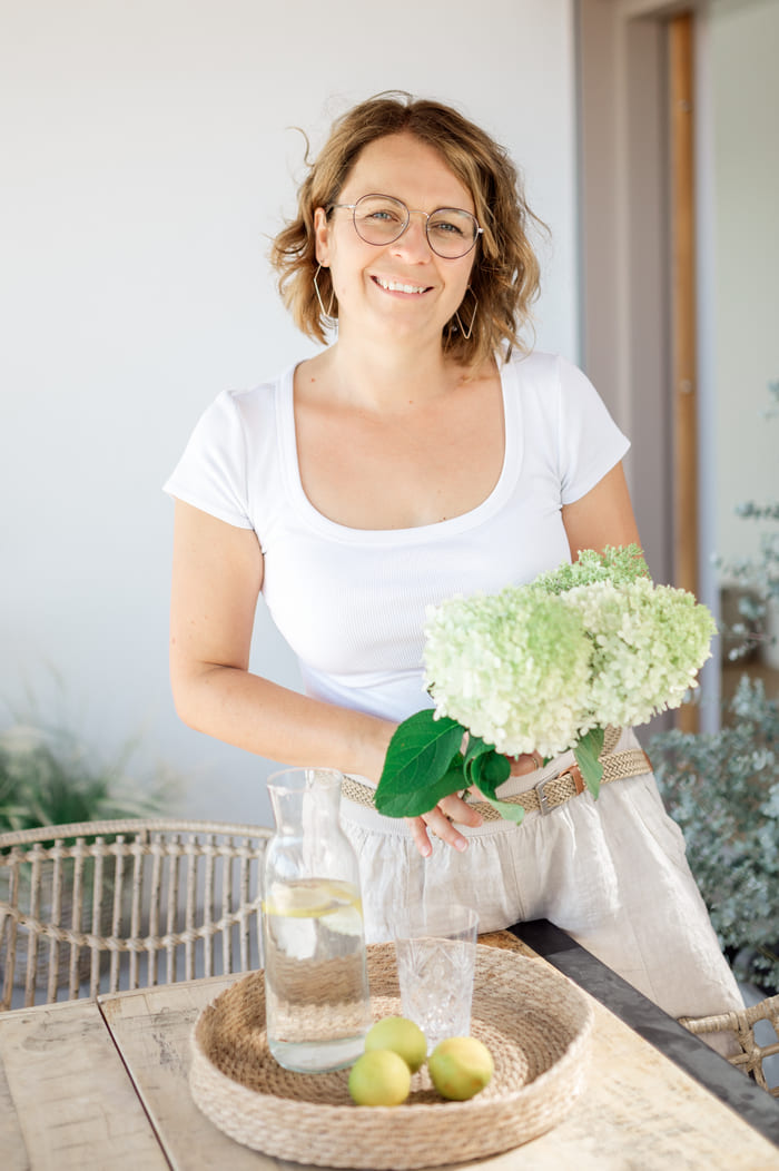 Melanie steht mit Blumen neben Tisch und erstellt Konzept für Raumgestaltung in Fürstenfeld.
